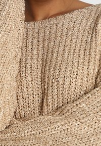 Béžový pletený svetr s volným střihem, s širokým výstřihem a vzorovaným, hrubým pletením se jemnými metalickými nitěmi.