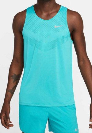 Mężczyzna w turkusowej bezrękawnikowej koszulce sportowej i pasujących krótkich spodenkach z małym logo Nike, stojący na jednolitym tle.