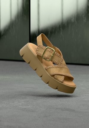 Sandales en cuir fauve avec une semelle plateforme épaisse en caoutchouc beige. Elles comportent plusieurs lanières et une boucle dorée en accent.