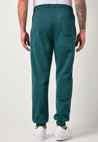 Tyrkysově modré tepláky s elastickým pasem, zúženými manžetami a zadní kapsou, doplněné o bílé tenisky. Měkká textura a ležérní design.