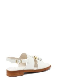 Sandalo in pelle bianca con suola in legno piatta, dotato di una cinghia alla caviglia regolabile e dettagli in metallo dorato. Design con punta aperta e dettagli a taglio.