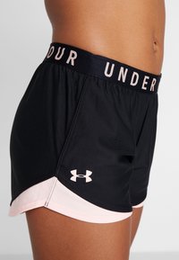 Black athletic shorts with a pink hem, featuring a wide black waistband labeled "UNDER" and a logo in the lower left corner.
