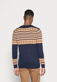 Pull en maille bleu marine avec des motifs géométriques orange et blancs sur les épaules et les manches, doté d'un col rond et de poignets côtelés.