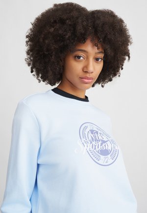Light blue sweatshirt with black neckline, featuring a circular graphic logo in purple and white, and a soft, smooth texture.