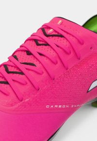 Zapatilla deportiva de color rosa brillante con cordones a juego, patrones de chevrones negros y parte superior texturizada etiquetada con "Carbon Infused" en texto blanco.
