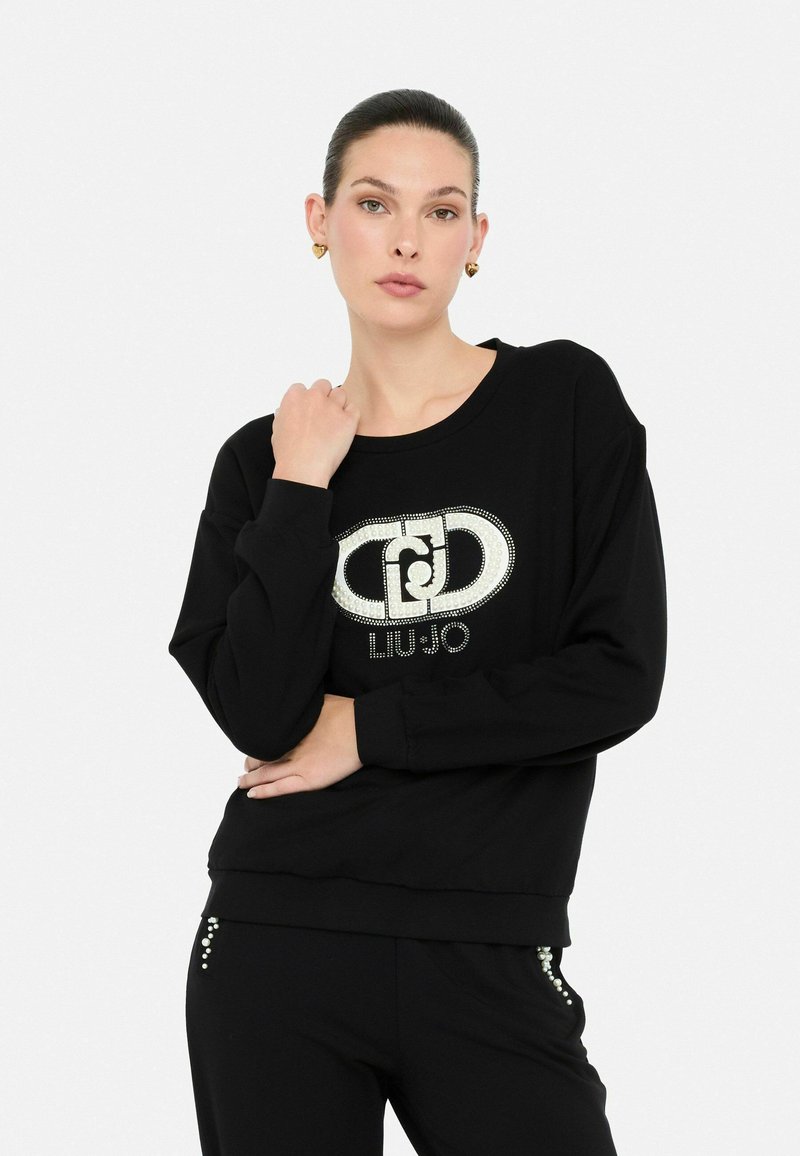 Musthave musta dressipluus pikkade varrukatega, ümmargune kaelus ja sädelev "LIU JO" logo. Pehme kangas, mugav lõige ja kaunistused pükstel.