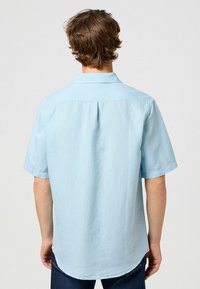 Chemise manches courtes bleu clair avec col, fabriquée en tissu texturé, dotée d'un pli au dos et d'un ourlet arrondi.