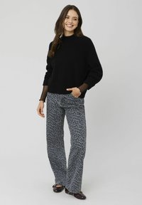 Sweater en maille noire avec un col montant et des manches transparentes, associé à un pantalon évasé gris à imprimé léopard. Des chaussures à enfiler marron complètent l'ensemble.