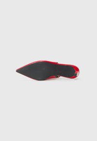 Chaussure à talon haut rouge avec un bout pointu, dessus en cuir verni brillant et semelle en caoutchouc noir avec un motif de grip texturé.