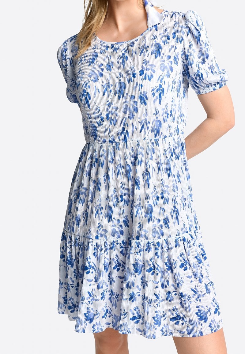 Vestido azul con estampado floral que presenta un diseño en capas, mangas cortas abullonadas y textura acanalada. La tela tiene un fondo blanco con patrones azules.