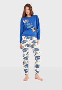 Sweatshirt bleu à manches longues mettant en avant des personnages de "Tom et Jerry", associé à un pantalon blanc orné de motifs répétés de "Tom et Jerry".