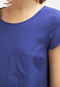 Top a maniche corte in tessuto blu reale solido, con tasca, scollo rotondo e texture liscia. Design semplice e aderente.