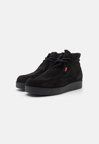 Bottines en daim noir avec bout rond, détails surpiqués, fermeture à lacets et semelle extérieure en caoutchouc noir texturé. Comprend une petite étiquette de logo rouge.