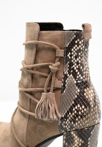 Stivale alla caviglia con punta in suede color caramello, lacci avvolti in suede con frange, e tacco e pannello posteriore in motivo pelle di serpente.