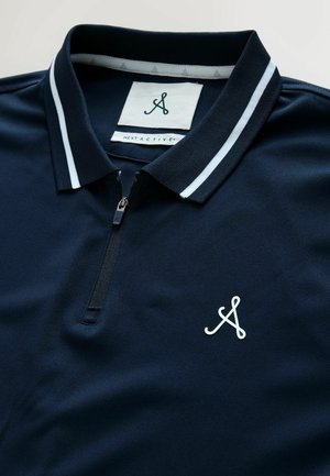 Marineblaues Poloshirt mit halbem Reißverschluss, weiß gestreiftem Kragen und weißem Logo. Hergestellt aus glattem, strukturiertem Stoff. Innenliegende Etiketten sichtbar.