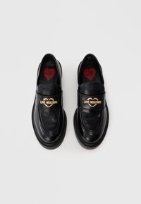 Mocassins de couro preto com uma fita larga com um detalhe em forma de coração dourado, bico redondo e interior almofadado com o logótipo vermelho "Love Moschino".