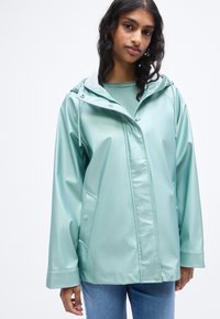 Αδιάβροχο μπουφάν σε μέντα πράσινο χρώμα με κουκούλα, διαθέτει κουμπιά τύπου σναπ, δύο πλαϊνές τσέπες και ομαλή, γυαλιστερή υφή.