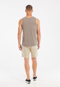 Grijze tanktop van katoen, gecombineerd met lichtbeige shorts. De outfit is casual, met een eenvoudige uitstraling en minimale details.