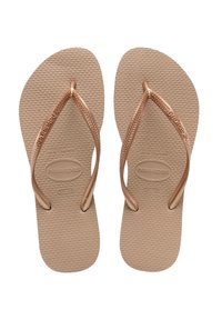 Tan gummifleksible flip-flops med en teksturert såle og rosegullremmer med vevd design. Merking synlig på sålen.