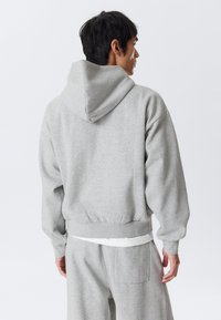 Lysegrå hættetrøje lavet af blødt materiale, med en afslappet pasform, en oversized hætte samt elastiske manchetter og kant. Udstyret med en kængurulomme.