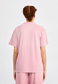 Roosa lühikeste varrukatega t-särk pehmest puuvillast, millel on lõdva lõike ja raglanvarrukad. Minimalistlik disain, ilma nähtavate mustrite või logo.