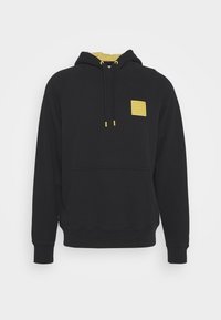 Sudadera negra con bolsillo frontal, forro amarillo en la capucha, puntas de cordón amarillas y un pequeño parche texturizado amarillo en el pecho.