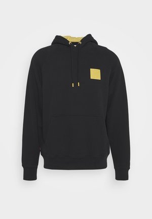Svart hoodie med framficka, gul huva foder, gul dragkedja tips, och en liten gul strukturerad fyrkantig patch på bröstet.