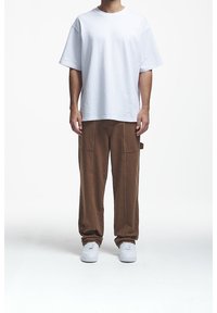 Biała, luźna koszulka z krótkim rękawem w połączeniu z brązowymi spodniami typu cargo. Spodnie mają boczne kieszenie i luźny krój, dopełnione białymi trampkami.