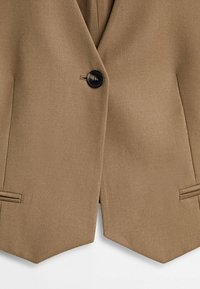 Blazer marron avec une fermeture à un bouton noir et deux poches à rabat horizontales sur le devant.