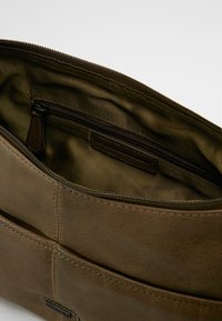 Ruskea nahkainen vetoketjullinen pussi, avoinna näyttäen kankaan vuorauksen sisäpuolella, jossa on sisempi vetoketjullinen tasku ja ompeluyksityiskohtia.
