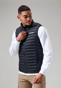 Zwarte gewatteerde puffer vest met een hoge kraag en ritssluiting aan de voorkant. Draagt over een wit langemouwen shirt. Logo weergegeven op de linkerborst.