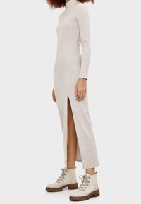 Lång, ljusbeige ribbad klänning med hög hals och sidoflik, som matchas med krämfärgade snörda ankelskor med en tjock sula.