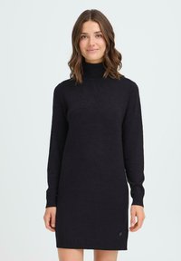 Knit črna obleka z visokim ovratnikom, dolgimi rokavi in sproščenim krojem. Vsebuje subtilno teksturo in majhen logotip na robu. Nastavljivi manšeti.