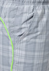 Gray plaid swim shorts with a lightweight fabric, elastic waistband, side pockets, and neon green accent along the seams.