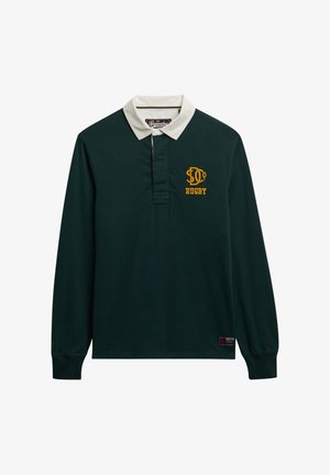 Camisa de rugby verde oscuro con mangas largas, cuello blanco y texto bordado en amarillo que dice "RUGBY". Cuenta con una tapeta y un parche del logo en el dobladillo.
