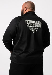 Sort langærmet træningsskjorte med "LIMITLESS STRENGTH" og "IRON ANVIL PROJECT" trykt i hvidt på ryggen. Glat tekstur.