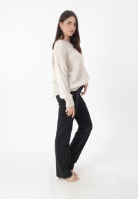 Maglione beige a maglia con una vestibilità rilassata e polsini a coste, abbinato a jeans neri a vita alta e a gamba larga, insieme a sandali leggeri con cinturini.