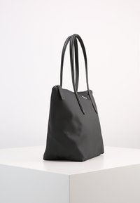 Sac fourre-tout noir avec une texture lisse, des poignées allongées et une fermeture éclair. Présente un motif subtil et un design épuré et minimal.