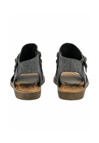 Sandalias de tela negra con un diseño texturizado, talón abierto y hebilla ajustable. Suela marrón claro con detalles de costura y plantilla acolchada.