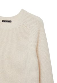 Crèmefarbener gestrickter Pullover mit rundem Halsausschnitt, gerippter Textur und Raglanärmeln, versehen mit einem kleinen Markenetikett am Kragen.