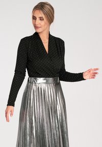 Czarny top z długim rękawem w białe kropki, zapinany w warstwach; połączony z błyszcząco metaliczną srebrną plisowaną spódnicą.