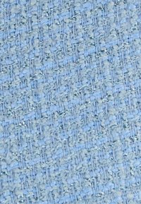 Lichtblauw gemêleerd stof met een geweven patroon van kleine lussen, wat zorgt voor een zachte en visueel interessante oppervlakte.
