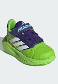 Green athletic shoe with a textured rubber upper, purple accents, reflective stripes, and a thick sole for cushioning. Features Velcro strap.