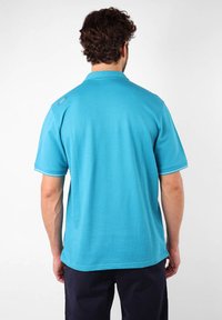 Chemise polo turquoise à manches courtes, col plat et finition contrastante sur les poignets. Tissu lisse, coutures visibles sur les épaules.