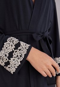 Marineblauwe robe met een tailleband, voorzien van kantversieringen op de mouwen. Zachte stof met een geprofileerd bloemenpatroon in crème.