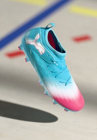 Scarpe da calcio con gradiente blu e rosa, con una parte superiore testurizzata, un design leggero, chiusura con lacci e un logo bianco prominente sul lato.