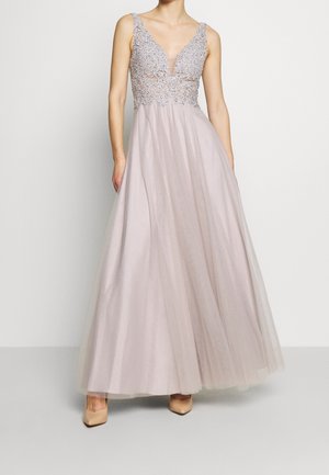 Ærmeløs lavendelfarvet kjole med dyb V-udskæring, blondeoverdel, flydende tylskørt, båret med nøgenfarvede spidse hæle på lys baggrund.