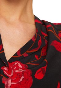 Tessuto nero con motivo di rose rosse, caratterizzato da un collo a V e una texture fluida, che mette in risalto i dettagli floreali intrecciati con steli sottili.