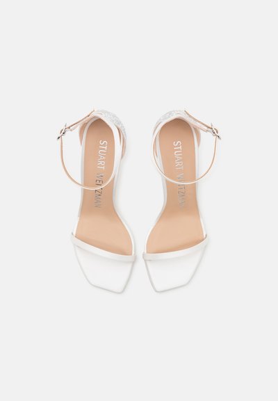 Sandales blanches à talons avec un bout carré, dotées d'une fine lanière à la cheville et d'une bande pailletée au talon. Fini lisse et satiné.