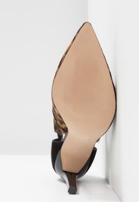 Chaussure à talon haut à bout pointu avec dessus imprimé léopard et semelle beige lisse, vue du dessous en angle contre une surface blanche.